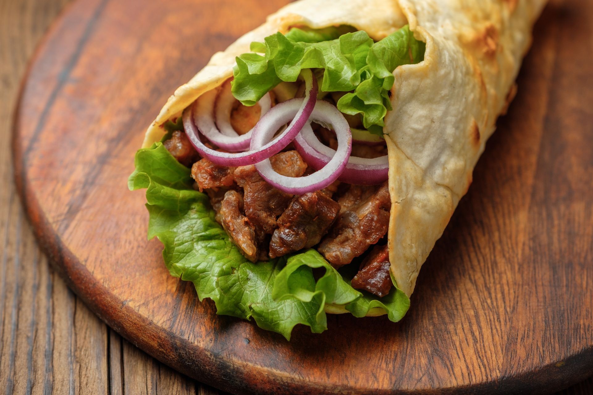 Doner kebab is lying on the cutting board.
Shawarma with meat, onions, salad lies on a dark old wooden table.